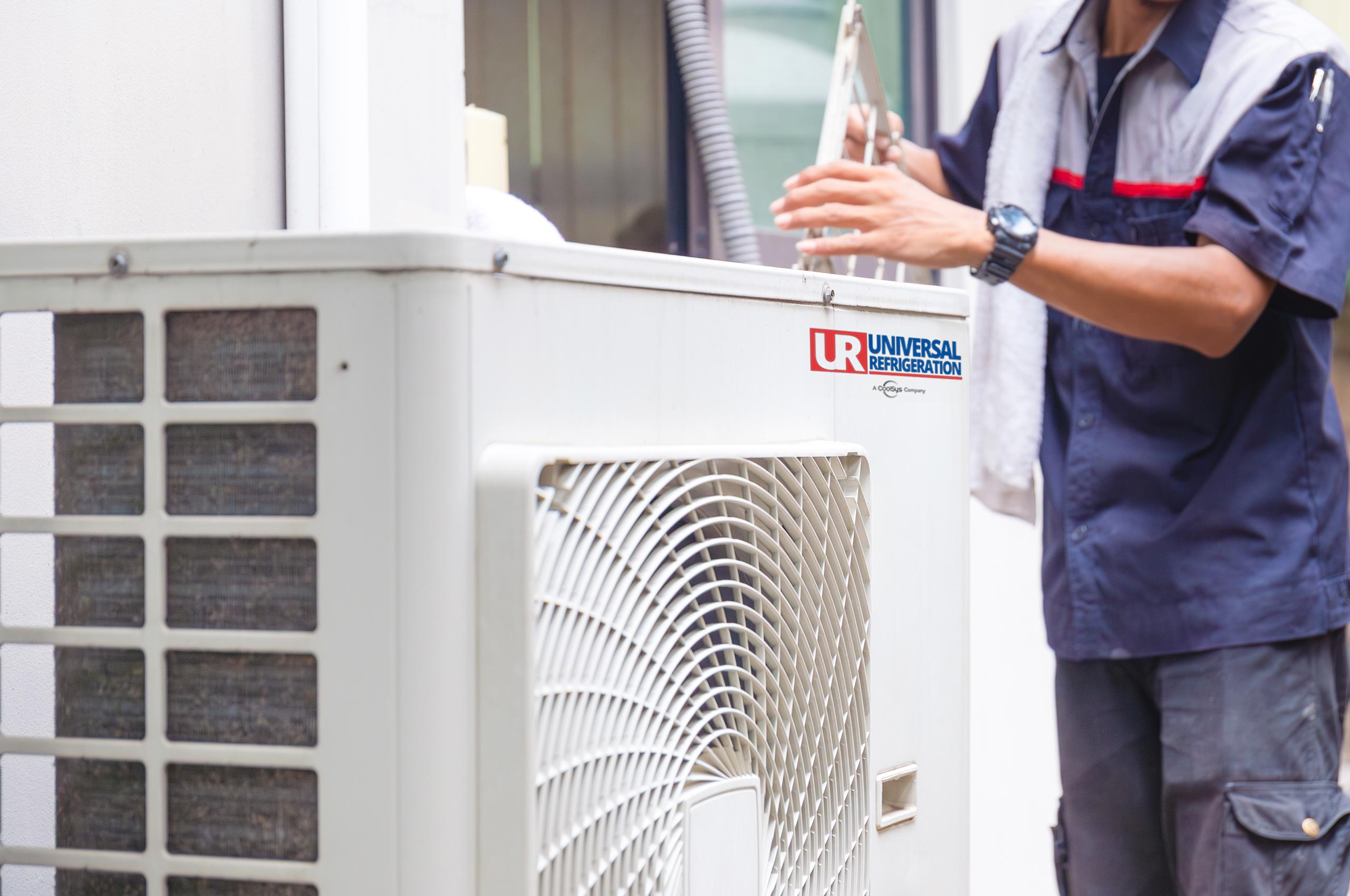 Technician completing HVAC maintenance on an outdoor air conditioning system to ensure it's functioning properly before the summer heat arrives. Contact Universal Refrigeration to get your HVAC system in tip-top shape!