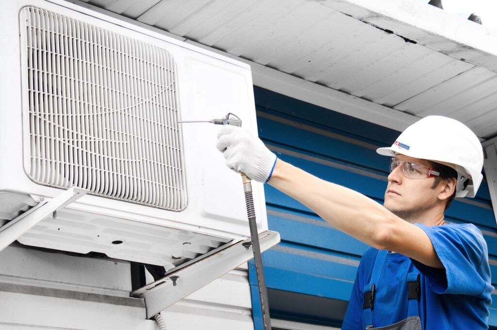 Universal Refrigeration Technician in white hard hat and blue shirt performing regular maintenance on a residential HVAC System